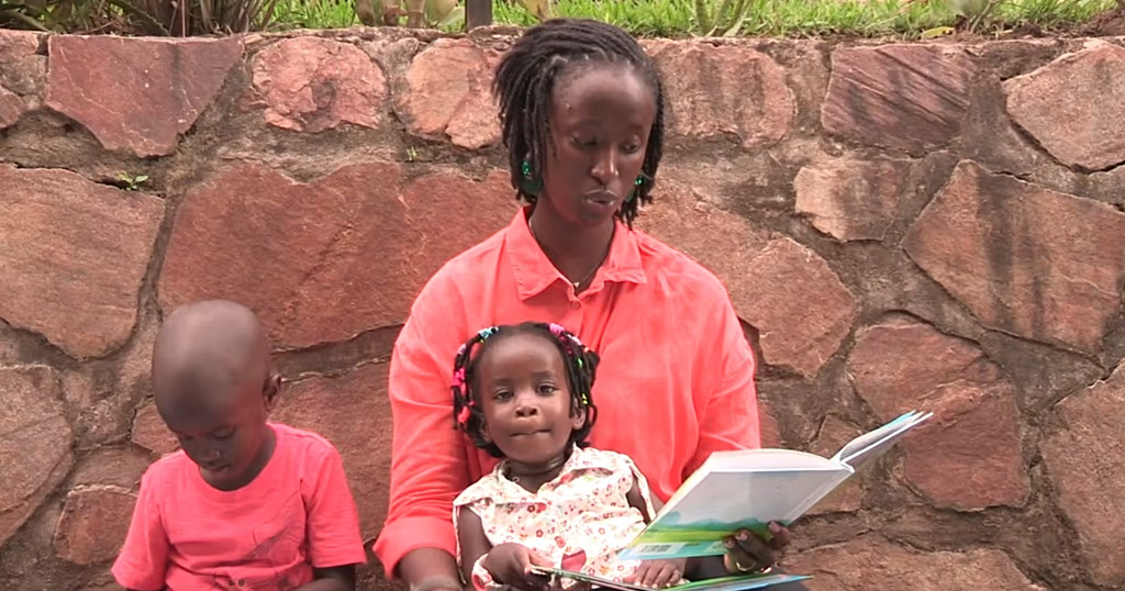 A mother reading a book to her two children outdoors
